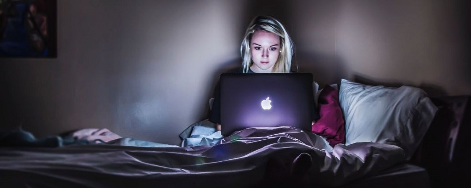 Frau arbeitet nachts im Bett sitzend an einem Laptop.